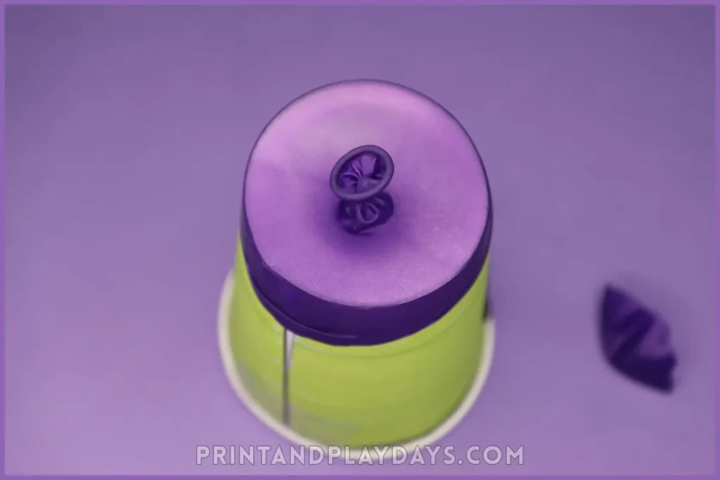a balloon with the tip cut off and stretched over a paper cup to make a pom pom shooter for kids