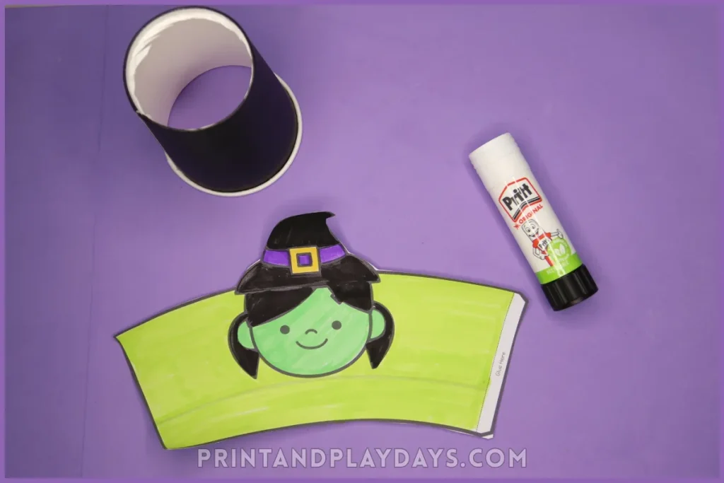Photograph of a paper cup, glue and a witch cup wrap to make a pom pom popper craft